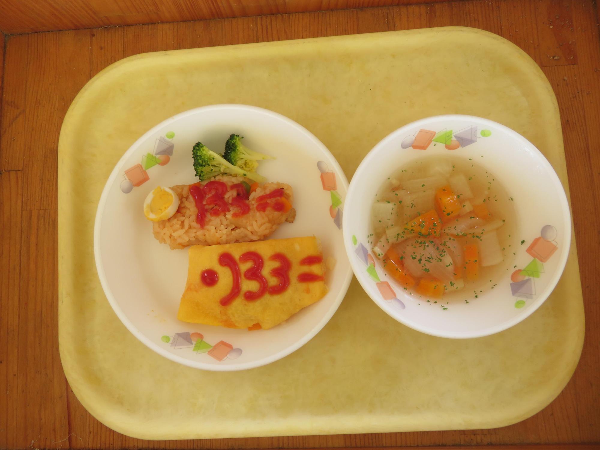 ケチャップでこいのぼりの絵を描いたハンバーグとオムライスにボイルしたブロッコリーが添えられたお皿とコンソメスープのお皿がトレーに乗っている写真