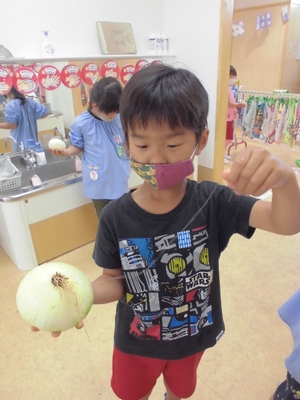 マスクを付けて大きな玉ねぎを片手に持った園児の写真