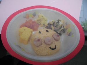 海苔とウインナーを使ってキャラクターの顔を作ったピラフと、卵焼きとサラダの給食の写真