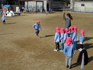 グラウンドで長縄跳びをする男の子と、順番を待っている子どもたちの写真