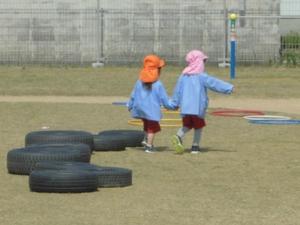 園内の庭を仲良く手をつないで歩く園児の写真