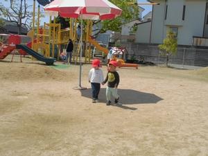 幼稚園の庭で仲良く手をつないで歩く園児の写真