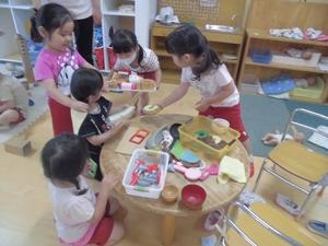室内の丸いテーブルを囲み、上に置かれたおもちゃを手にとって遊ぶ5人の子供たちの写真