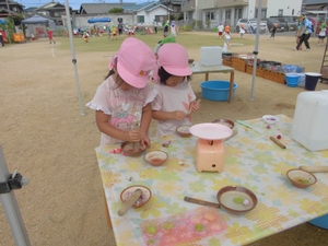 校庭のテーブルに置かれた小さなすり鉢で、女の子2人がホウセンカをすり潰している写真