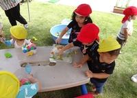 氷の中に入っている花をとろうとしている赤色の体操帽を被った園児の右横で氷に右手を伸ばす同じ帽子を被った女児の写真