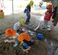 水が流れている様子を上から眺めている3歳児クラスの女児とその左横で左手の人差し指で水の方を指差す先生の写真