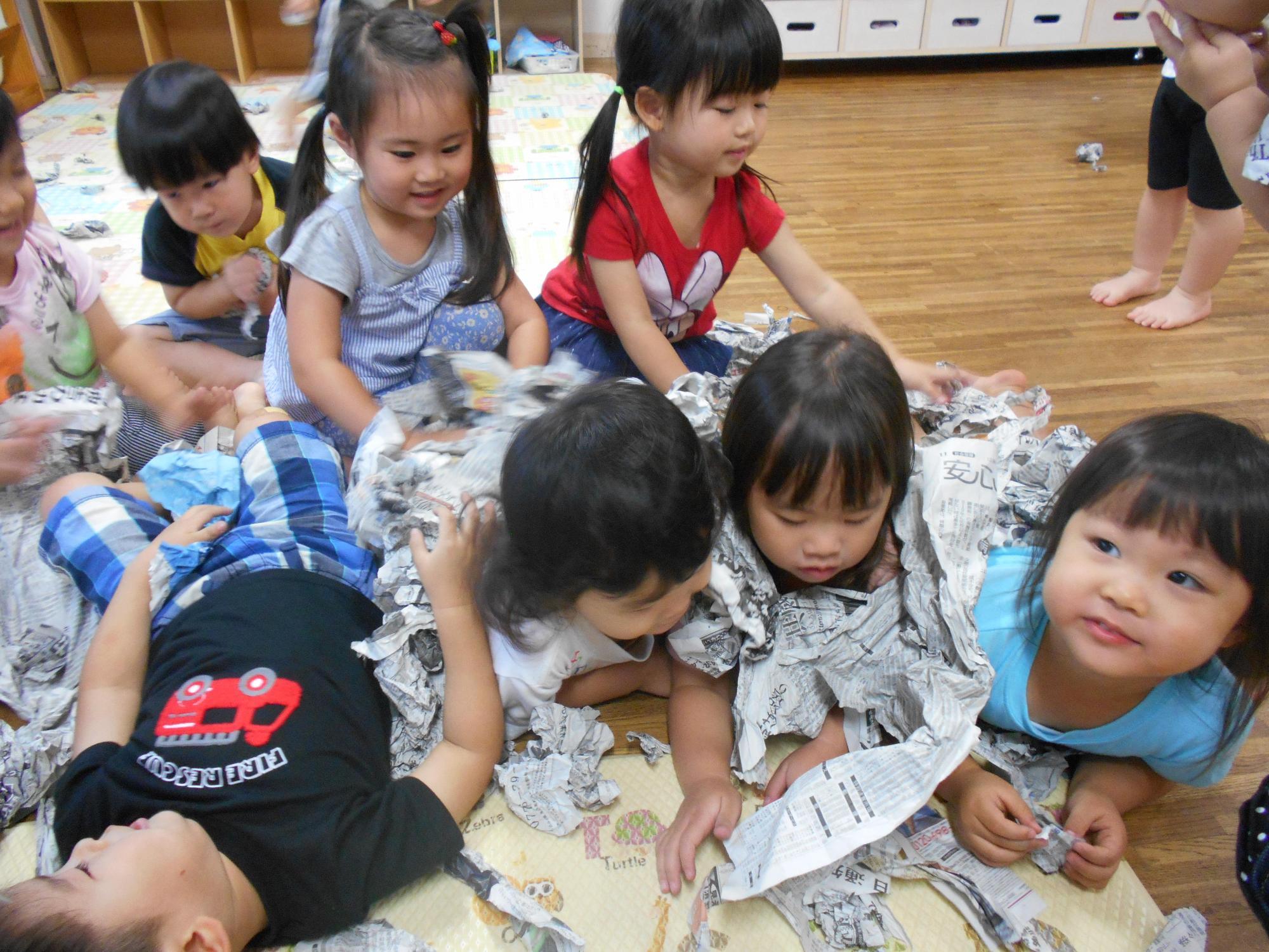園内の教室で新聞紙を身体に巻いたり敷いたりして楽しそうに遊ぶ園児たちの写真