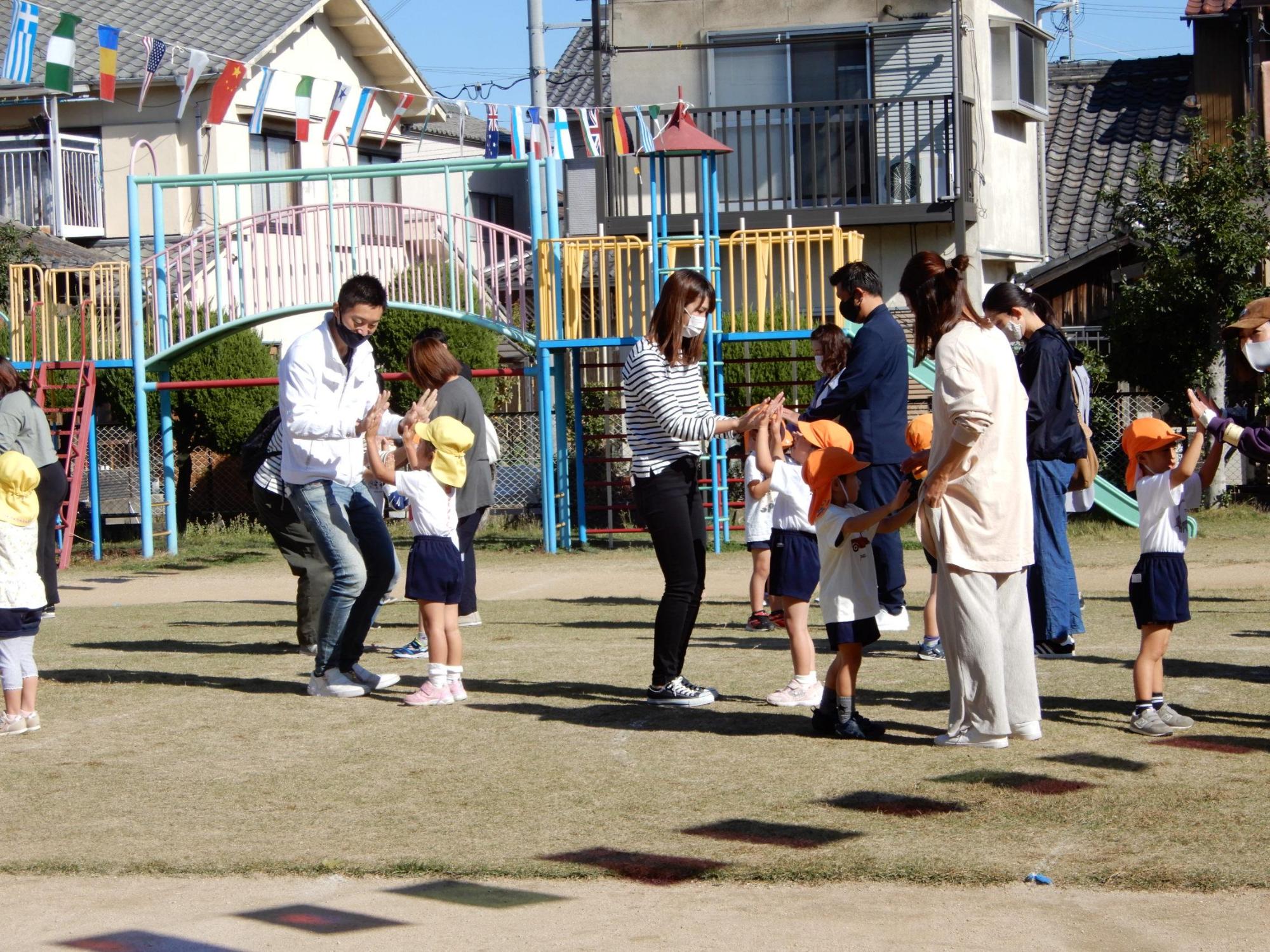 運動会で保護者と向き合って楽しそうに両手を合わせる3歳児クラスの園児の写真
