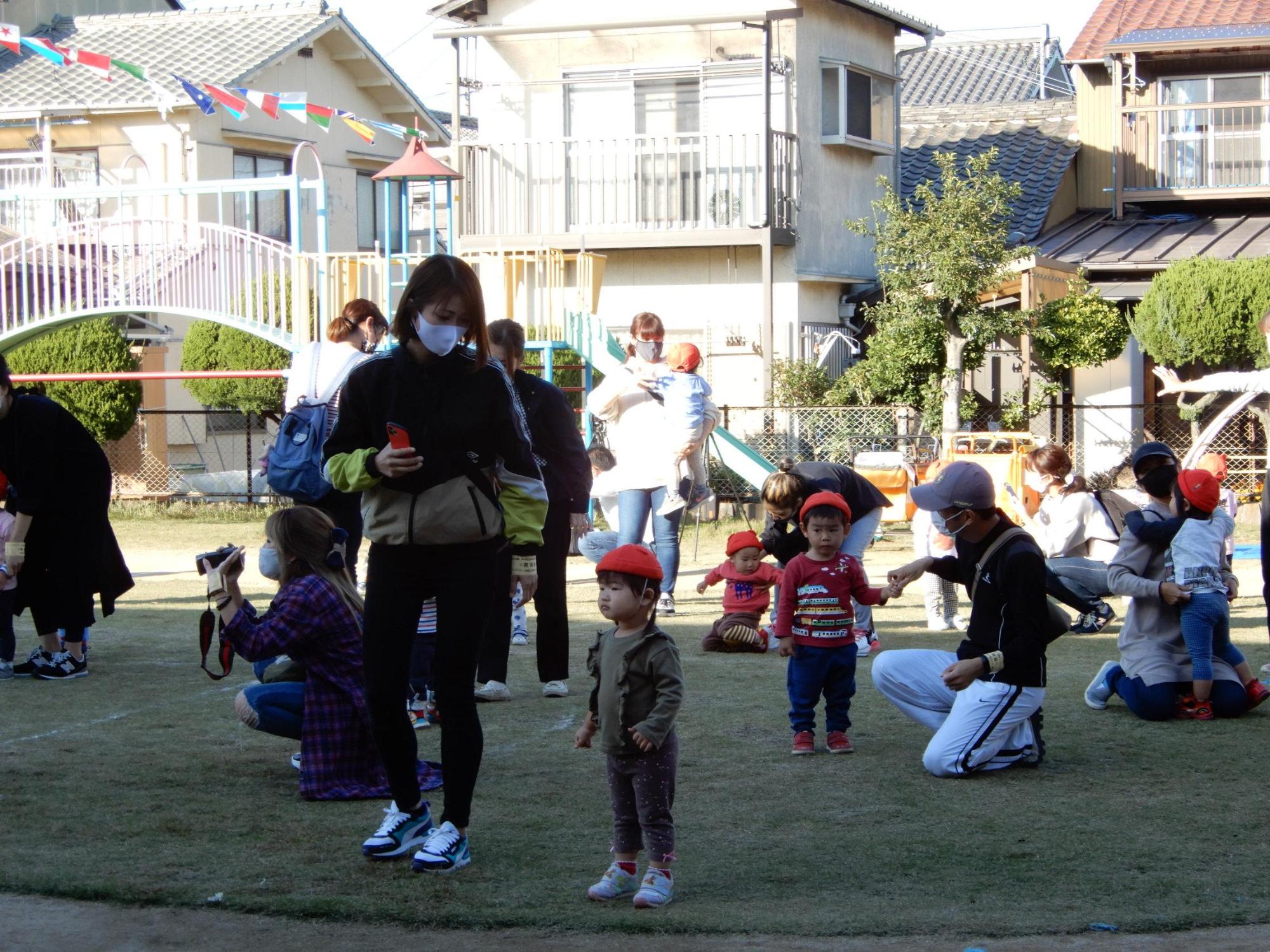 万国旗の下で保護者に抱っこしてもらったり手を繋いでもらったりしている園児たちの写真