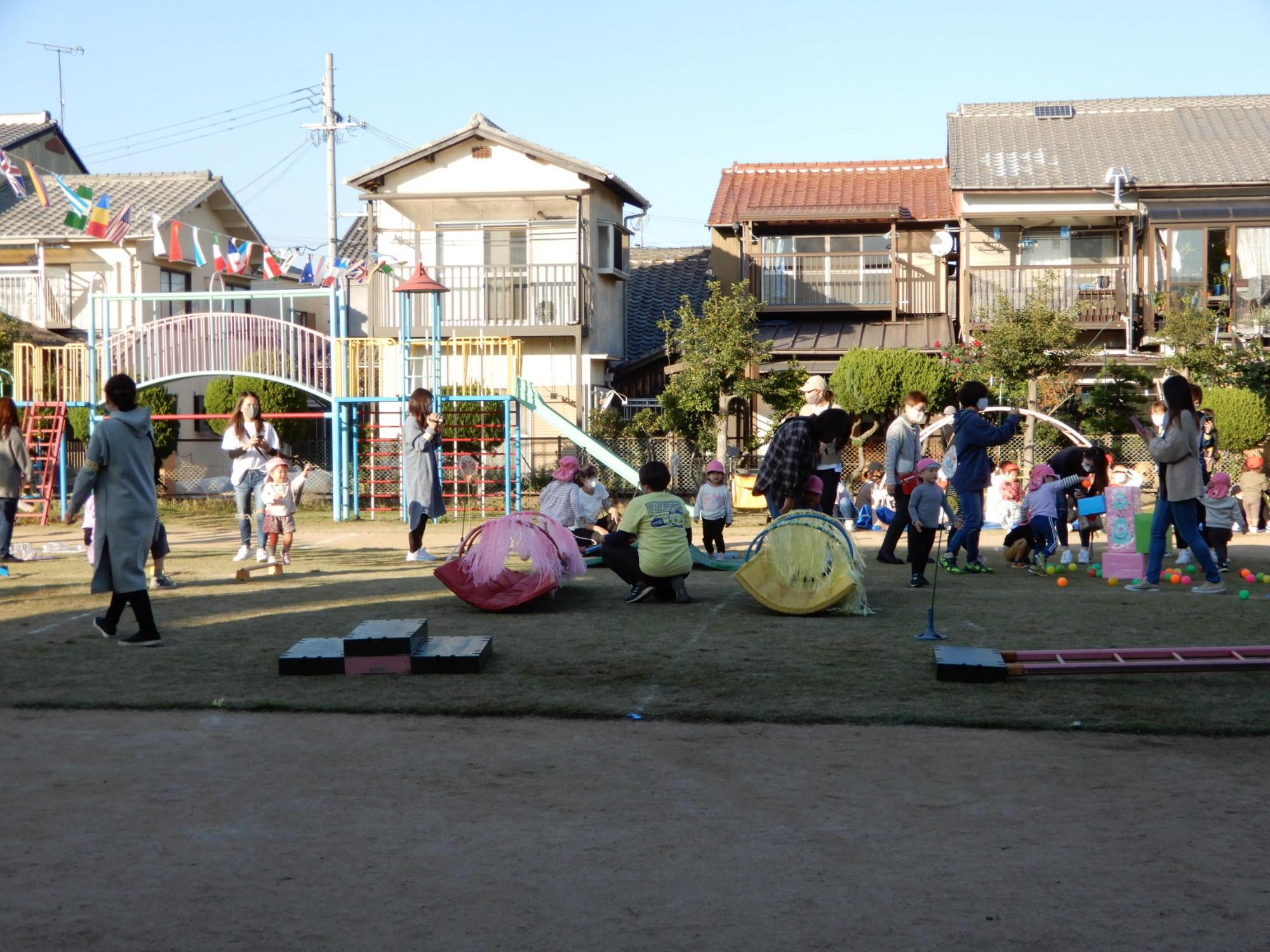 様々な障害物が置かれた障害物競走を楽しみながらおこなう園児たちの様子を見守る保護者の写真