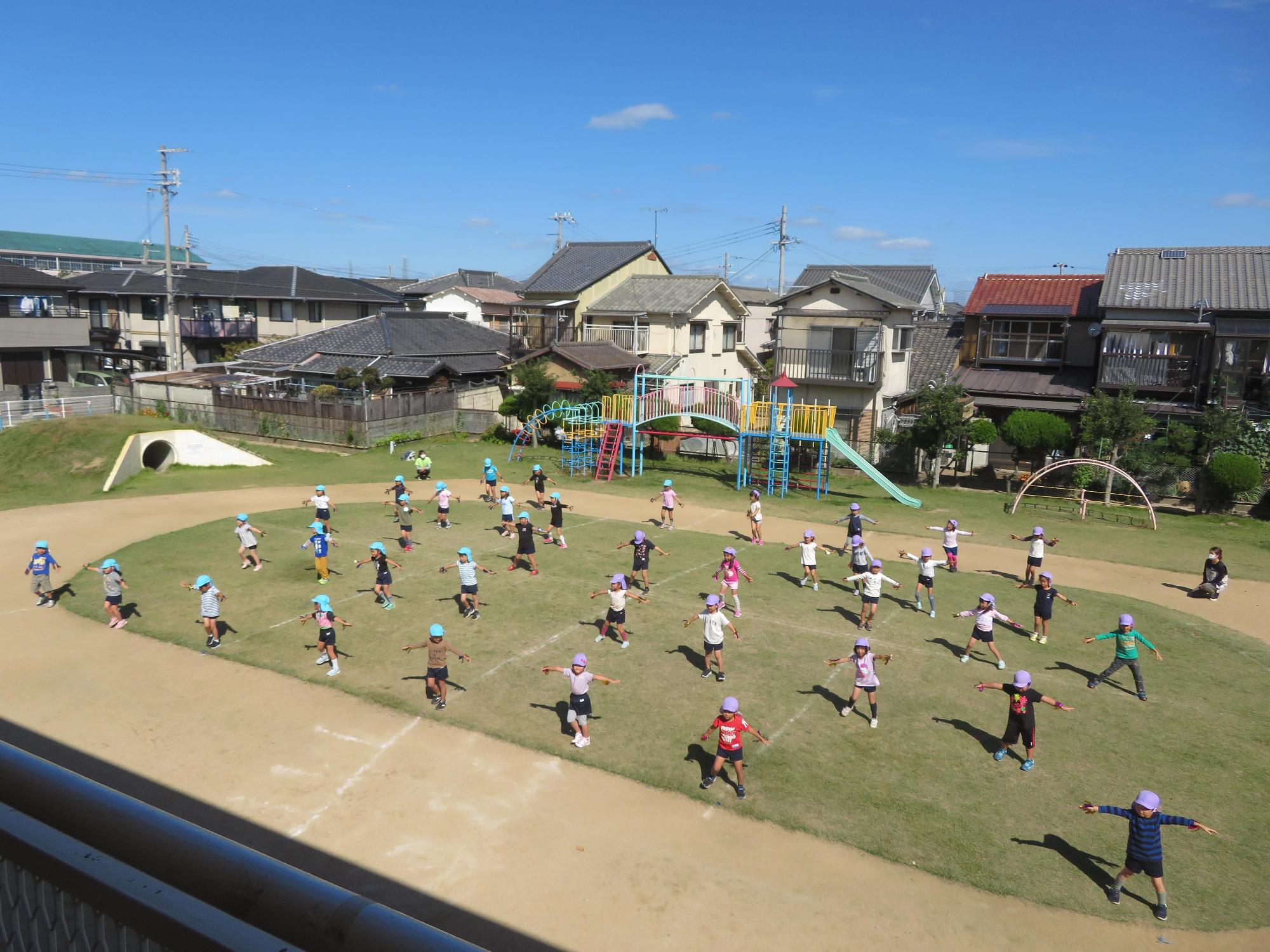 両手を目一杯広げて運動会のオープニング体操をする園児たちを上空から撮影した写真