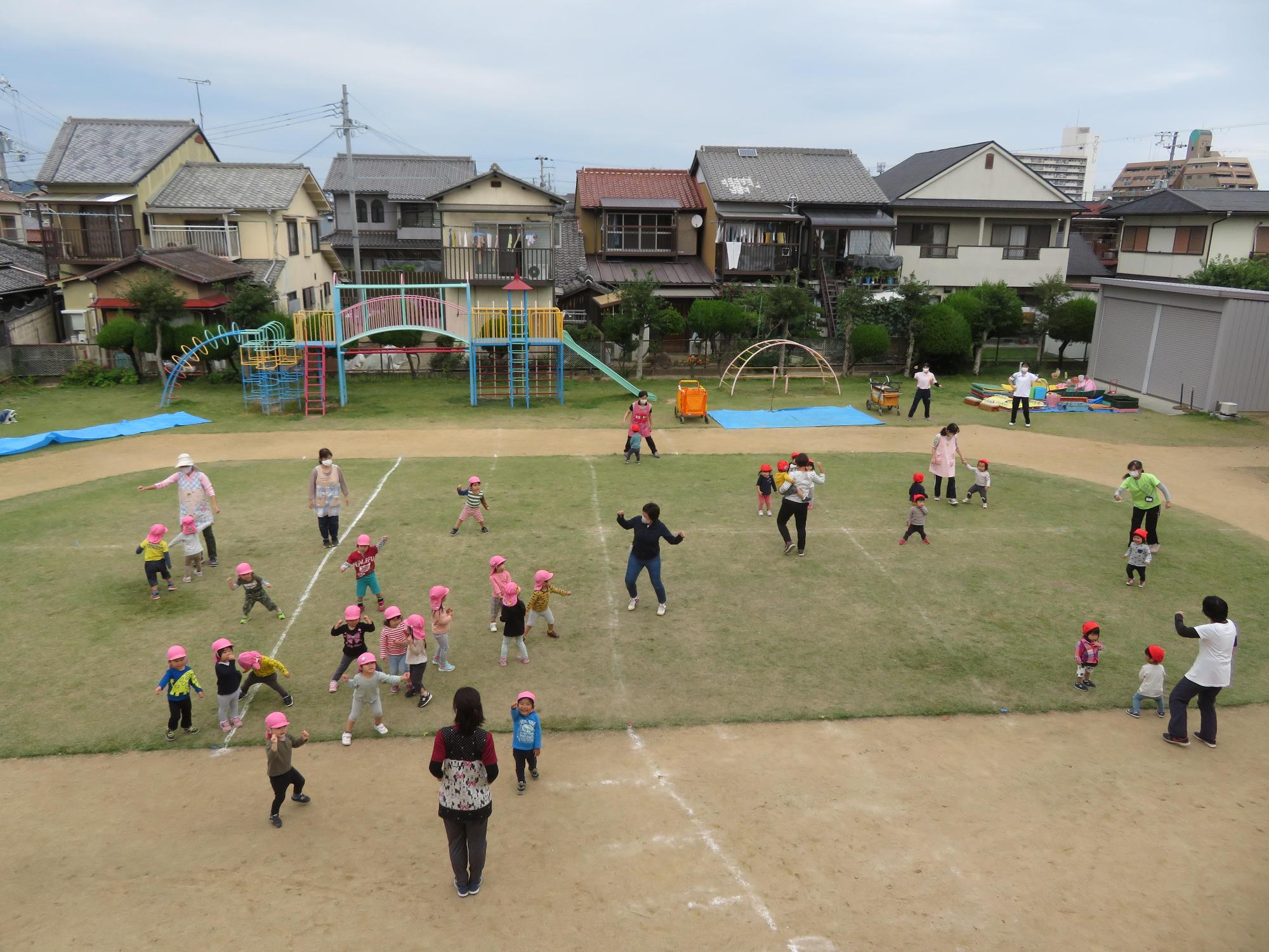 先生たちと一緒にサンサン体操をする1歳児2歳児クラスの園児たちを上空から撮影した写真