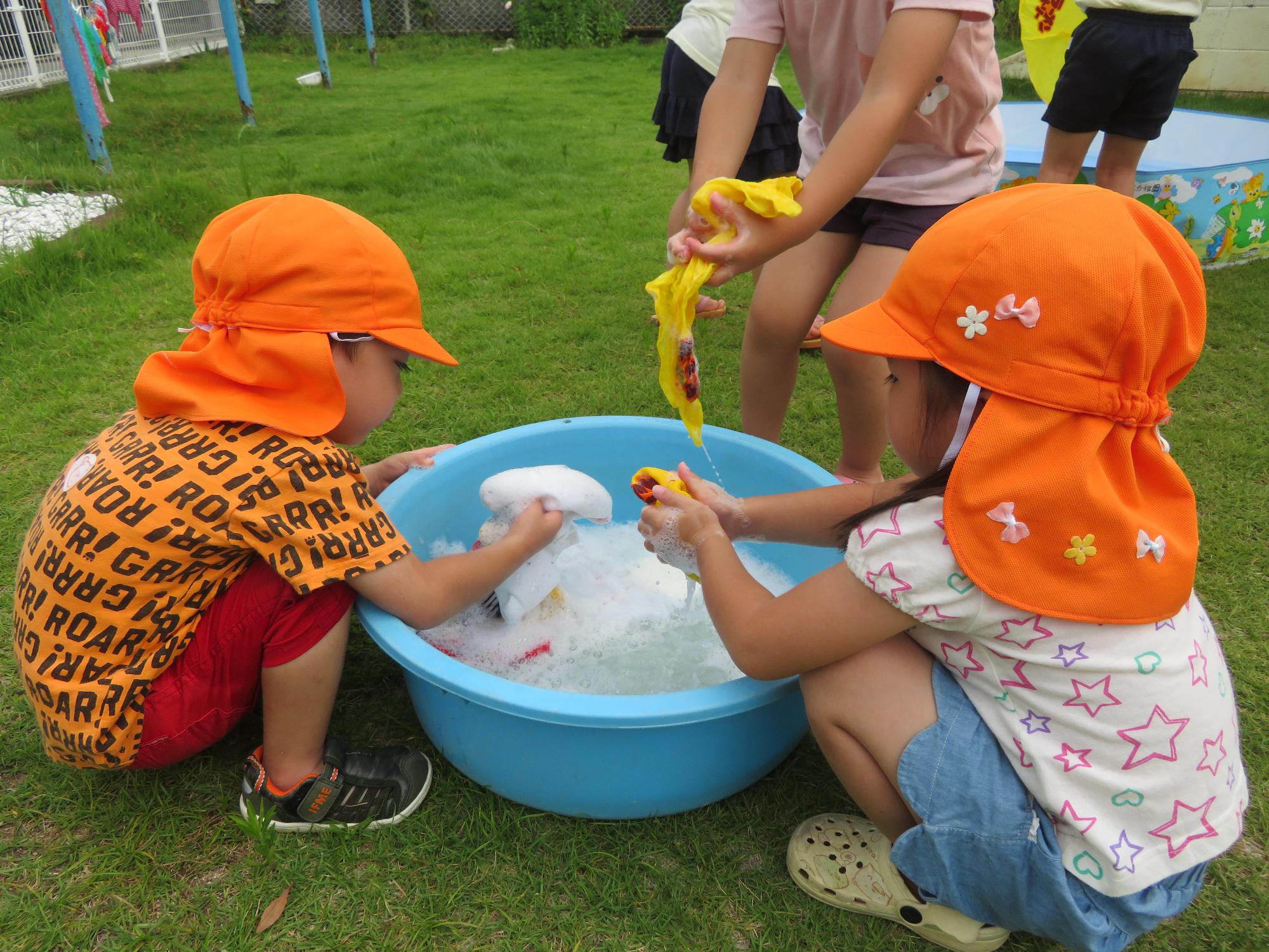 大きな洗面器に入った泡だらけの洗濯物を一生懸命洗う園児3人の写真