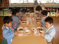高砂児童学園内の教室で机を並べて向かい合って黙々と給食を食べる園児たちの写真