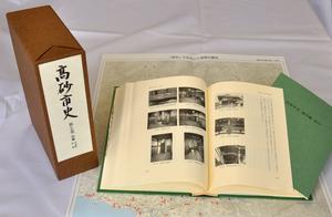 高砂市史第七巻「別編 文化財・民俗」のサンプル写真。展開された地図の上に小冊子、見開きになったハードカバーの本、直立した函等が配置されている