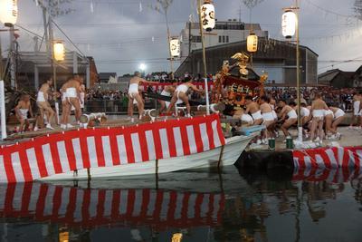 大勢の人々が見守る中神輿を船に運んでいる船積みの様子の写真