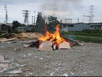 砂利の敷地の中で木の板などを焼却している様子の写真