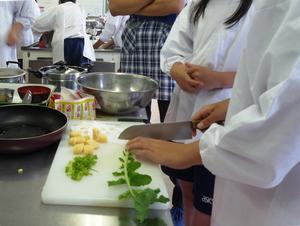 米田西小学校でのエコクッキングにおける調理中の写真で、まな板の上大根の葉を刻んでいる。