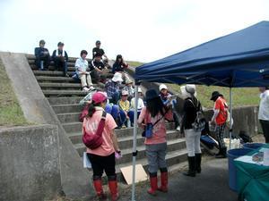 土手に設けられた階段に座りながら階段下の前田真里さんの説明を聞く参加者たちの写真