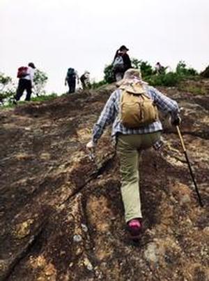 トレッキングポールを片手に急な岩肌を登る参加者の写真