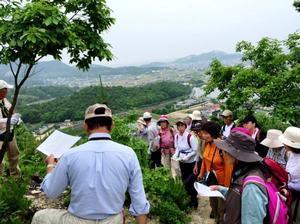 高御位山の上で資料を見ながら説明をする松本先生と、それを聞く参加者たちの写真