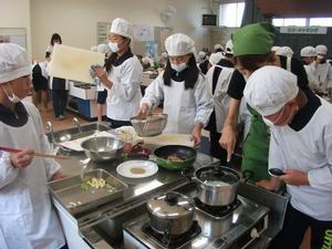 実習中の調理台の1つを撮影した写真。炒め物をしたり、まな板を拭いている児童たちが写されている。
