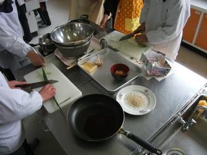 エコクッキングの中で児童たちが調理をしている調理台の写真。野菜を刻んでいる調理台にはフライパンやボウルなどが並べられている。