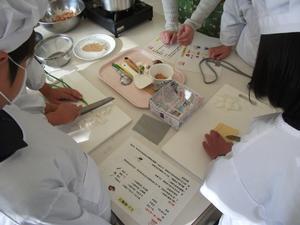 調理をしている児童たちの手元の写真。2人が食材を細かく刻んでおり、その脇で見ている児童たちの手元が写されている。