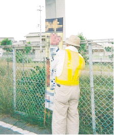 道端のフェンスに設置されている違反広告物と、点検している作業員の写真