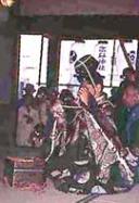 人々が見守る中、和服の装束の男性が正座している祭礼の様子の写真