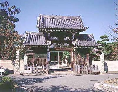 石垣や石塔に挟まれて門を開ける十輪寺入口の写真