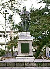 木々を背景に立つ工楽松右衛門の銅像の写真