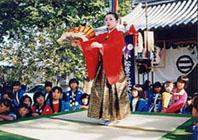 赤い法被と金の袴の扇子を持って舞踊をしている人の写真