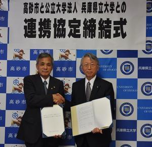高砂市長と兵庫県立大学の職員の男性が協定書を持って握手をしている写真