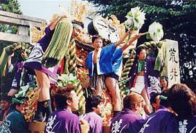 お祭りで神輿の上に乗り盛り上げる人たちの様子の写真