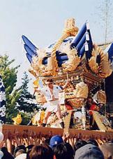 青と金色の神輿の中央に人が乗っている写真