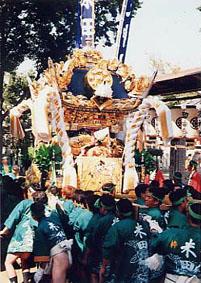ハッピを着た数十人の男たちが、背丈3メートルほどもある金色に光った神輿を担ぐ様子の写真
