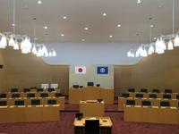 中央に議長の席、左右に4人掛けの議員席、手前に質問席が移っている無人の議会の写真