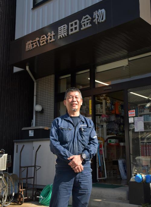 金物屋の前でにこやかに立つ男性の写真