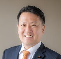 黒いスーツ姿で正面を向いている笑顔の松野優也議員の写真