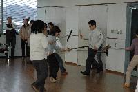 屋内にて、刃物を持つ人を刺又を持つ職員数名が壁に押さえつける訓練の写真