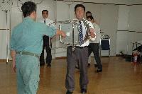 屋内にて、刃物を持った人の攻撃に対して椅子を盾にして身を守る訓練の写真