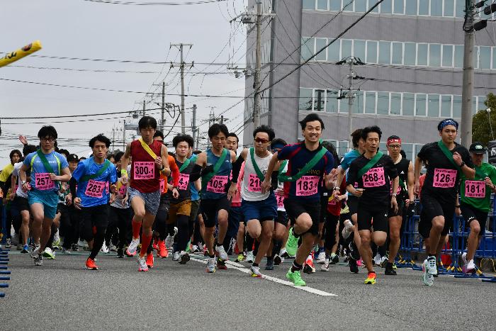 舗装された道で横並びになって一斉に走り出す大人のランナーたち